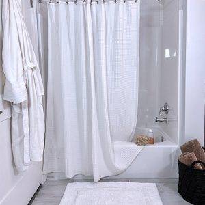 Stevens & Olivier white waffle shower curtain with white tufted bath mat in bathroom